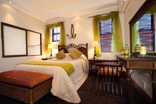 a bedroom with a bed and a desk and windows at Rise and Shine Lodge in Bloemfontein