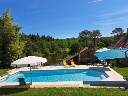 une piscine avec deux parasols et une maison dans l'établissement Le moulin, à Saint-Yrieix-la-Perche