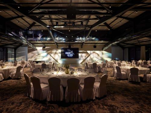 a banquet hall with white tables and chairs and a television at Domaine du Liziec Vannes - MGallery Collection in Vannes