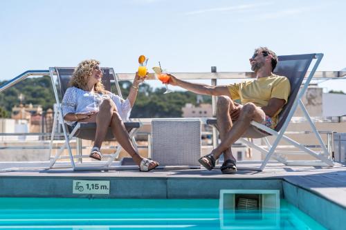 a man and woman sitting in chairs next to a swimming pool at Onmood Cala Ratjada - Bed & Brunch in Cala Ratjada