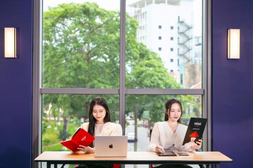 two women sitting at a table with books and a laptop at Wink Hotel Hai Phong - 24hrs Stay in Hai Phong