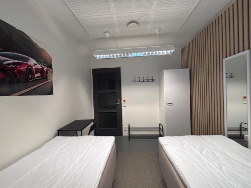 a bedroom with two beds and a painting of a car on the wall at Kotimaailma - Vihtyisä Hostelli in Kokkola