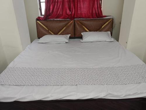 a large bed with white sheets and a red curtain at Radhika P Guest House Ajmer in Ajmer
