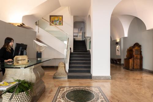 a woman standing at a desk in a hallway with a staircase at Hotel Principe Di Villafranca in Palermo
