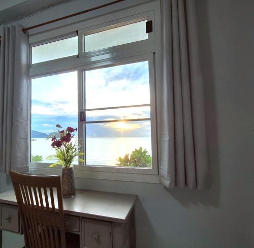 a window with a desk and a chair looking out at the ocean at Sunrise Guesthouse in Prachuap Khiri Khan