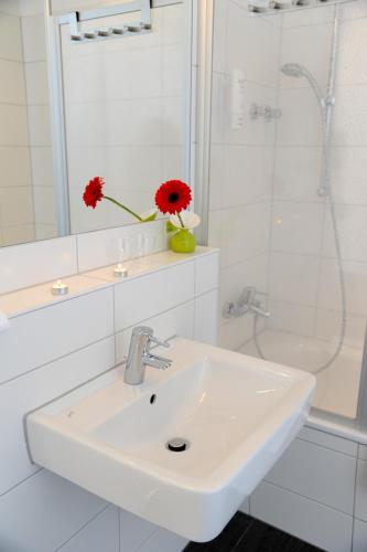 a white bathroom with a sink and a vase with a red flower at H+ Hotel 4Youth in Berlin