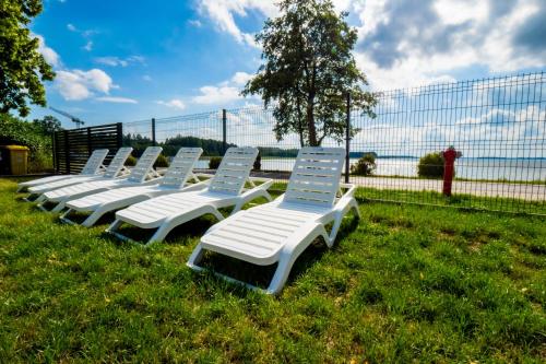 a row of white lounge chairs sitting in the grass at Mazurskie Apartamenty "Jak Tu Miło!" in Węgorzewo
