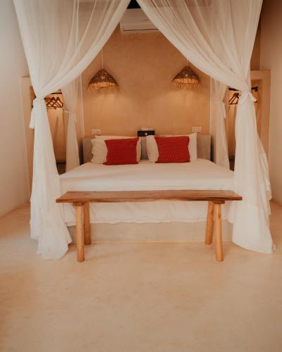 a bedroom with a bed with curtains and a bench at Monkey Suites in Diani Beach