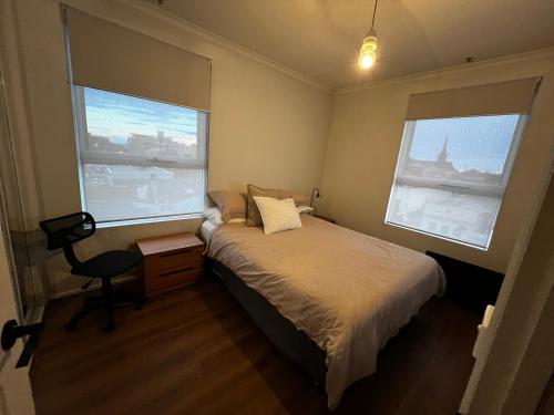 a small bedroom with a bed and two windows at The Ryrie Loft in Geelong