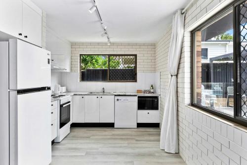 a white kitchen with white appliances and a window at Salt & Stone Villa on the beach - Villa 2 in Burrum Heads