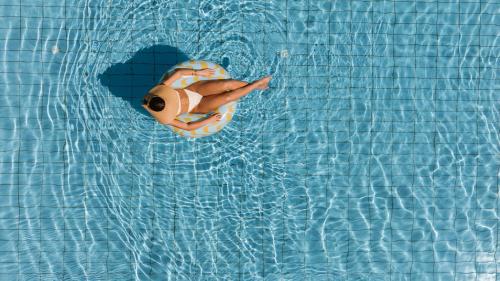 a person in a swimsuit floating in a swimming pool at Ammos Boutique Apartments & Suites in Malia