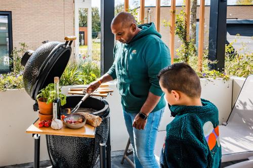 a man and a boy cooking food on a grill at Recreatiewoning 'Steenpatrijs' op Gemoedelijk Vakantiepark in Voorthuizen