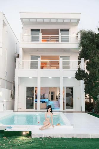 a woman sitting on the edge of a pool in front of a house at Hi Yang Seaview Villa in North Pattaya