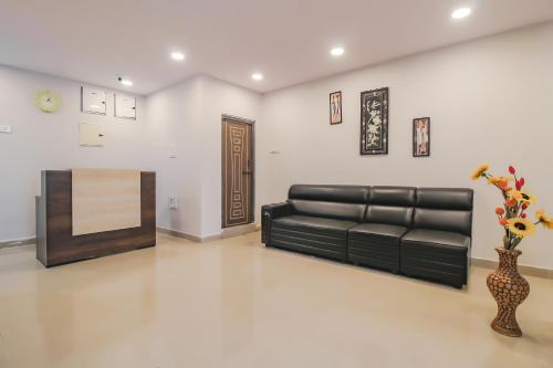a living room with a black leather couch and a vase with flowers at SPOT ON Pnd Complex in Hyderabad
