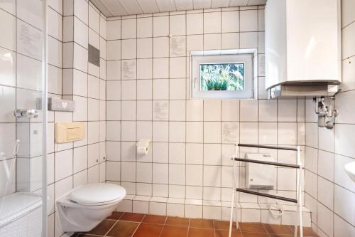 a white tiled bathroom with a toilet and a window at Haus Am Sonnenhügel in Bad Urach