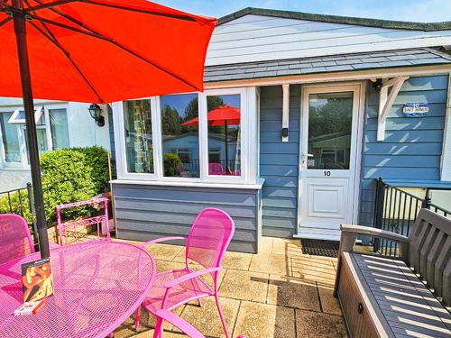 a table with pink chairs and a red umbrella at Dart Haven - cheerful holiday bungalow in Galmpton in Galmpton-on-the-Dart