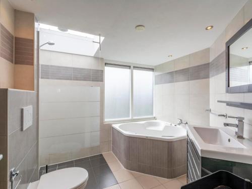 een badkamer met een wastafel, een bad en een toilet bij Spacious Villa with garden in Callantsoog