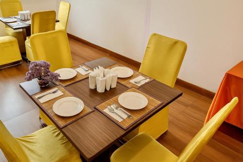 a dining room table with yellow chairs and a table with plates at Hotel Kian by JMD Group in New Delhi