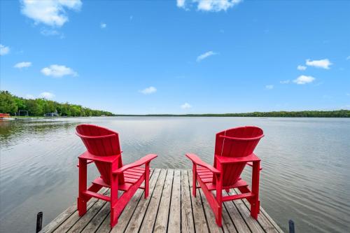 two red chairs sitting on a dock on a lake at Lakeview Loft A-frame Escape Tobermory in Tobermory