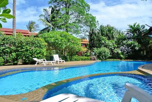a large swimming pool with two white chairs and trees at Luxurious Thai-Style Villa with a Swimming Pool Just 20 Meters from Beach Access in Ban Bang Po