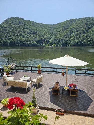 two people sitting on a deck with an umbrella at Casa Golful Mraconiei Eselnita in Eşelniţa