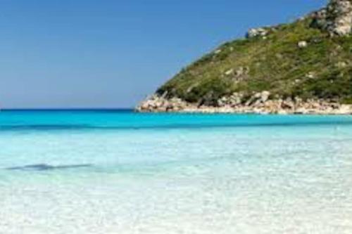 a beach with blue water and a mountain in the background at Beautiful luxury villa located in Sardinia in Villasimius near the beaches in Gesturi