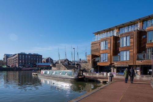 a couple of people walking on a dock next to a river at Boat House - Luxe Apt with River View - Next to Harbour & Cafes in Bristol