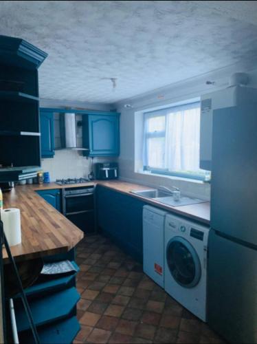 a blue kitchen with a sink and a washing machine at Surrey Hills Retreat - 2-Bed - Easy London Access in Ash