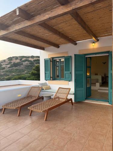 a patio with two chairs and a porch with green shutters at Lipsi Blue Hotel in Lipsoi