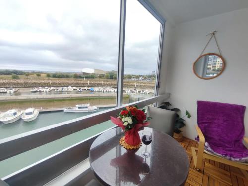 a room with a table and a window with boats in the water at Appartement vue sur mer & le port de Courseulles-sur-Mer in Courseulles-sur-Mer