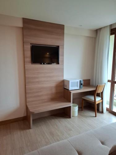 a living room with a tv and a desk with a microwave at Vista Azul Apart Hotel - Suítes com vista para a mata de pinheiros in Pedra Azul