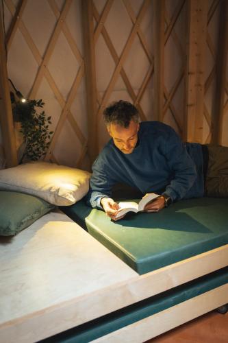 a man sitting on a bed reading a book at Cozy Yurt in the Woods in Sainte-Agathe-des-Monts