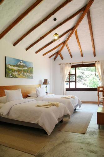 a bedroom with two beds and a ceiling with beams at Hotel Claroscuro Casa Ilayaku in Guangopolo