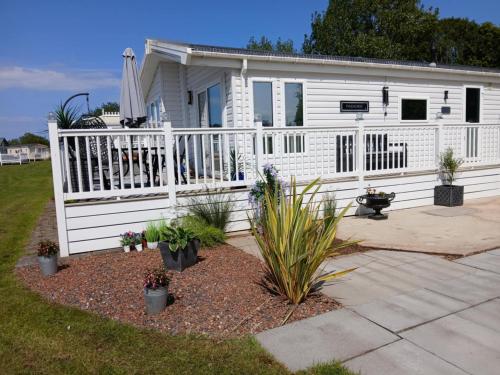 a white house with a white fence and plants at Sea Breeze, Vintage 90, Luxury 2 bed Lodge, Skegness, 2 dogs max, Contractors Welcome - East Coast Holidays in Lincolnshire