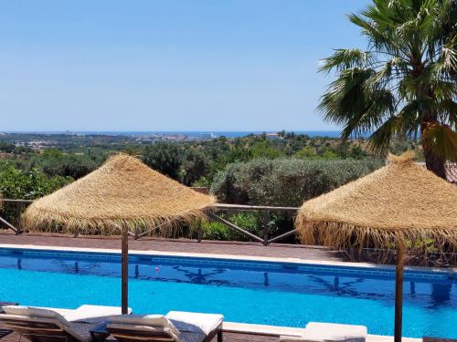 a swimming pool with straw umbrellas and chairs at Retiro da Janela in Boliqueime