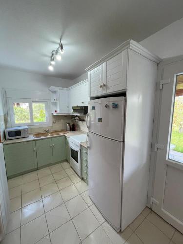 a kitchen with white cabinets and a white refrigerator at Entire villa with big garden and BBQ amenities in Áyios Pávlos