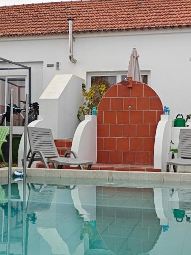 a swimming pool with two chairs and a red brick wall at Casinhas Vale de Mouro in Melides