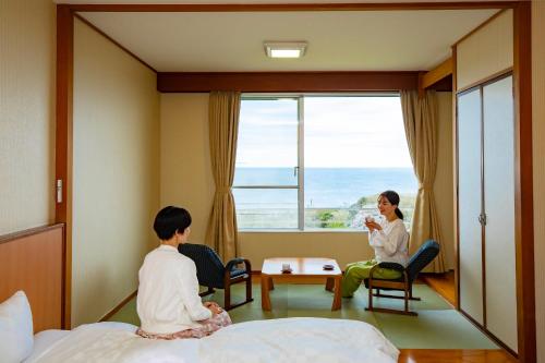 a boy and a woman sitting on a bed looking out the window at Kyukamura Echizen-Mikuni in Sakai