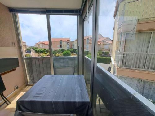 d'un balcon avec une table et une grande fenêtre. dans l'établissement Appartement 2 pièces avec loggia aménagée à Marseillan-Plage - FR-1-326-863, à Marseillan