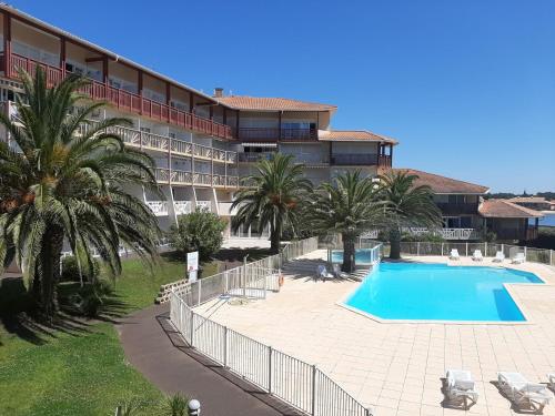 un complexe avec une piscine, des palmiers et un bâtiment dans l'établissement Appartement Duplex T2 avec Piscine à Vieux-Boucau, Proche Plage - FR-1-239-769, à Vieux-Boucau-les-Bains