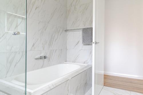 a white bathroom with a tub and a glass shower door at Large Premium Family Getaway with Centralised Heating in Shepparton