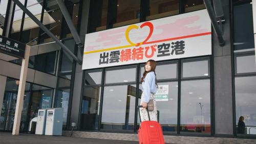 a woman standing in front of a building with a red suitcase at Matsue Excel Hotel Tokyu in Matsue