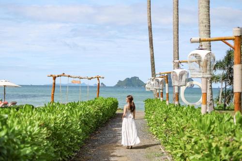 a woman in a white dress walking down a path next to the ocean at Tinidee Hideaway Tonsai Beach Krabi - SHA Extra Plus in Tonsai Beach