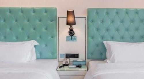 a bedroom with two beds and a green headboard and a lamp at Xana Lite Anqing Yuexi Swan Squre Branch in Yuexi