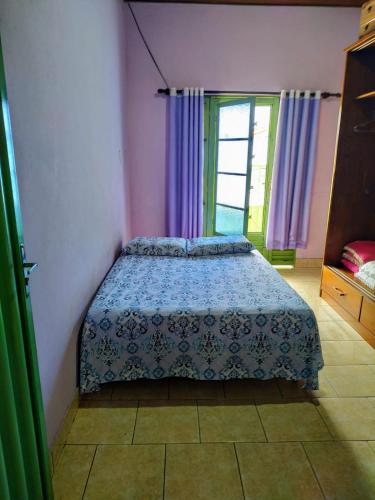 a bedroom with a bed and a window with purple curtains at Espaço Sinara in Jaraguá