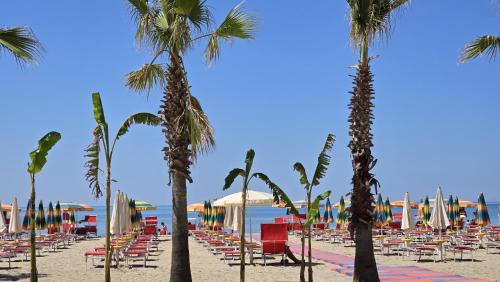 a beach with chairs and palm trees and the ocean at Hotel Virginia in Durrës
