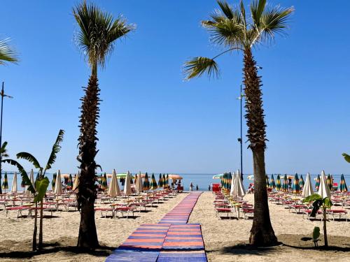 a beach with chairs and palm trees and the ocean at Hotel Virginia in Durrës