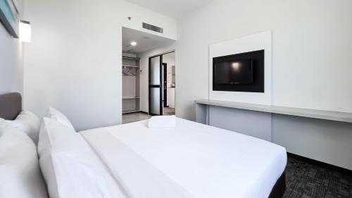 a white bedroom with a bed and a tv at Amansari Hotel Nusajaya in Nusajaya