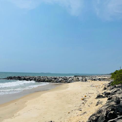 a beach with rocks and the ocean on a sunny day at Kaustubha beach villa in Udupi