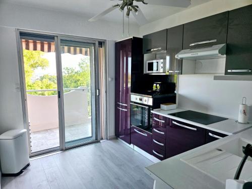 une cuisine avec des armoires noires et une grande porte coulissante en verre dans l'établissement T2 Vue Mer avec Grande Terrasse & Parking 4 min Plage - SpiritofFamily06, à Cagnes-sur-Mer